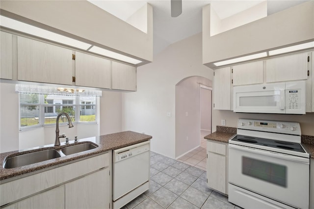kitchen with a sink, white appliances, arched walkways, light tile patterned floors, and lofted ceiling