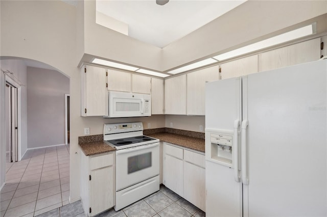 kitchen featuring dark countertops, arched walkways, white appliances, and light tile patterned flooring