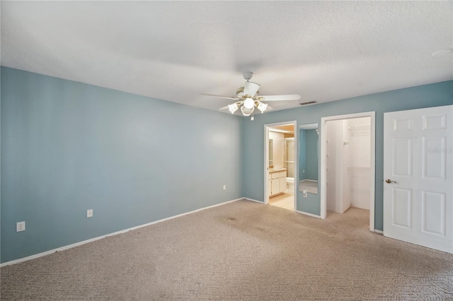 unfurnished bedroom with baseboards, a closet, connected bathroom, a spacious closet, and light carpet