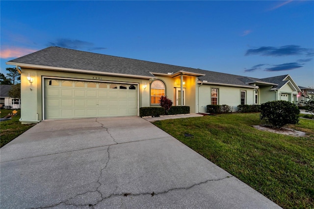 ranch-style home with driveway, a garage, a front lawn, a shingled roof, and stucco siding