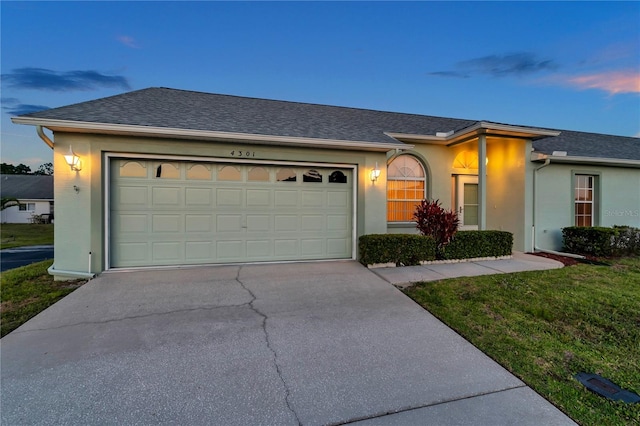 ranch-style home with a shingled roof, an attached garage, stucco siding, a yard, and driveway