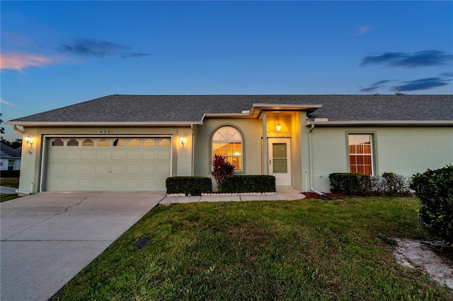 ranch-style house featuring roof with shingles, stucco siding, concrete driveway, an attached garage, and a yard