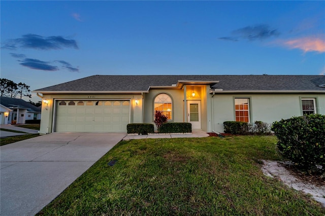 ranch-style home with a garage, stucco siding, a shingled roof, concrete driveway, and a lawn