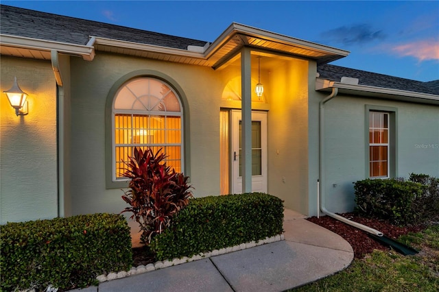 property entrance featuring a shingled roof and stucco siding