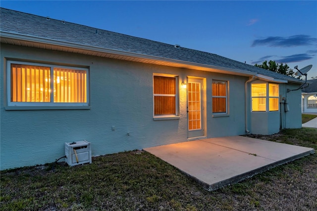 back of house featuring roof with shingles, stucco siding, a yard, and a patio area