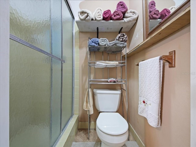 bathroom with toilet, a stall shower, and baseboards