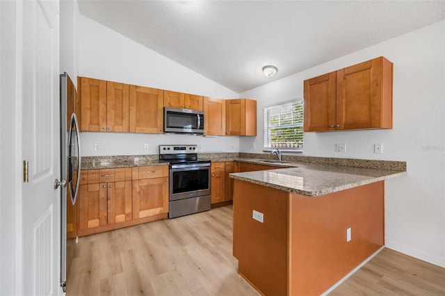kitchen with light wood-style floors, appliances with stainless steel finishes, stone counters, a peninsula, and lofted ceiling