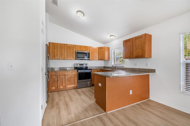 kitchen featuring a peninsula, stainless steel appliances, light wood finished floors, and a sink
