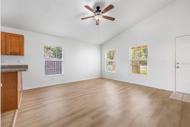 unfurnished living room featuring light wood finished floors, baseboards, high vaulted ceiling, and ceiling fan