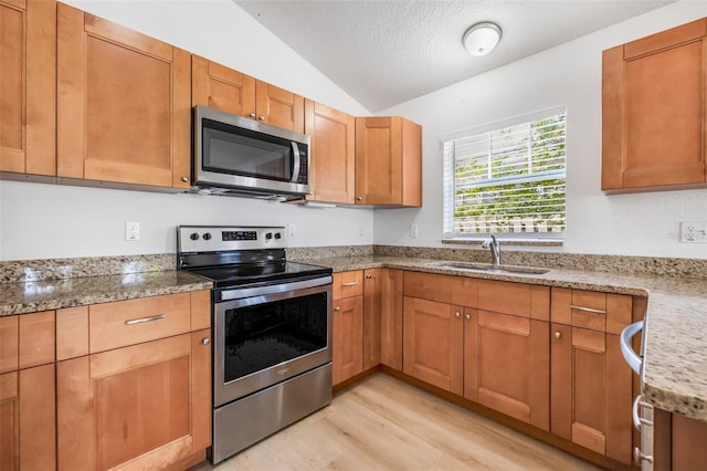 kitchen with lofted ceiling, a sink, light stone countertops, light wood-style flooring, and appliances with stainless steel finishes