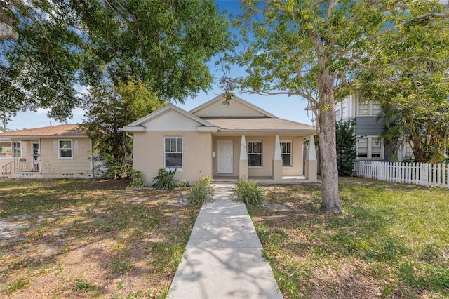 view of front of house featuring stucco siding, a front lawn, fence, and covered porch