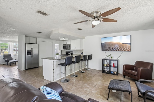 living area with a ceiling fan, a textured ceiling, visible vents, and light tile patterned floors
