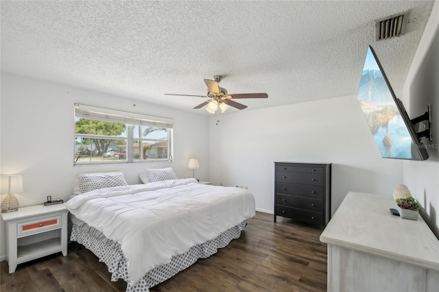 bedroom featuring a ceiling fan, a textured ceiling, visible vents, and dark wood-type flooring