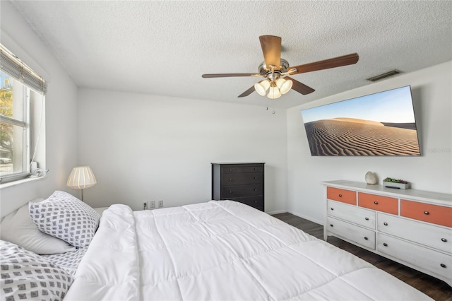 bedroom featuring a ceiling fan, a textured ceiling, visible vents, and dark wood-type flooring