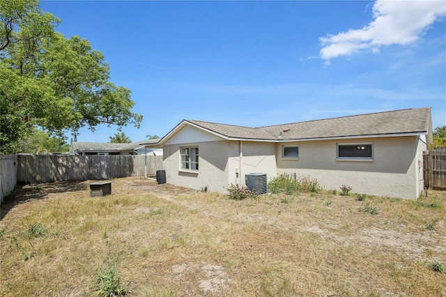 rear view of house with central AC, a fenced backyard, roof with shingles, and stucco siding