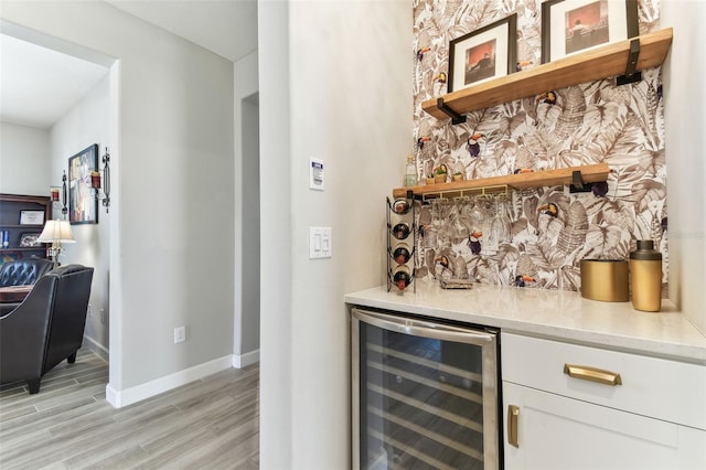 bar featuring beverage cooler, a bar, baseboards, and light wood-style flooring