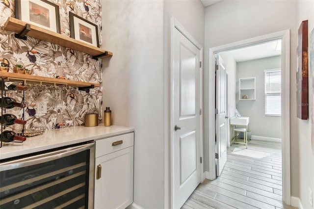 bar featuring light wood finished floors, a dry bar, wine cooler, and baseboards