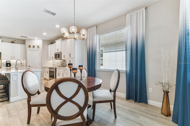 dining space featuring visible vents, light wood finished floors, baseboards, and a notable chandelier