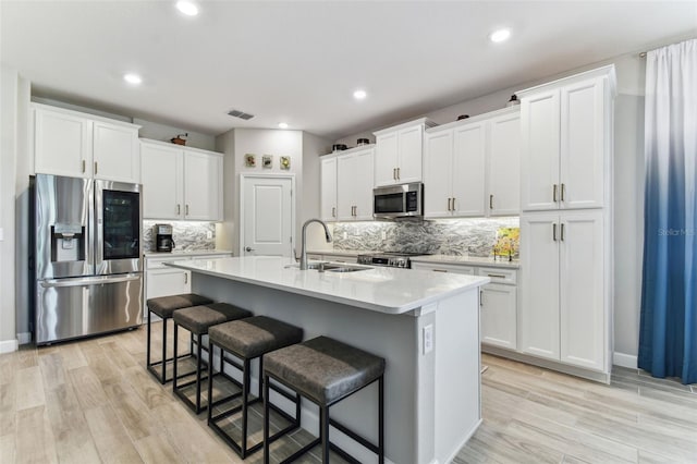 kitchen featuring decorative backsplash, a breakfast bar, white cabinets, appliances with stainless steel finishes, and visible vents