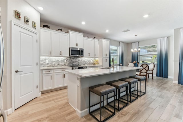 kitchen with a sink, a chandelier, light wood finished floors, stainless steel microwave, and visible vents