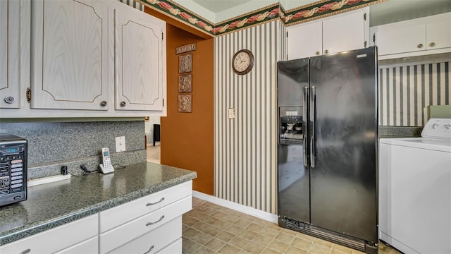 kitchen featuring black fridge with ice dispenser, washer / dryer, white cabinetry, and baseboards