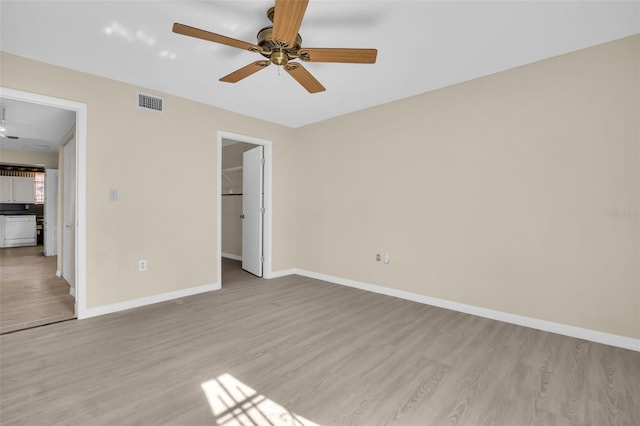 unfurnished bedroom with light wood-style floors, baseboards, a spacious closet, and ceiling fan