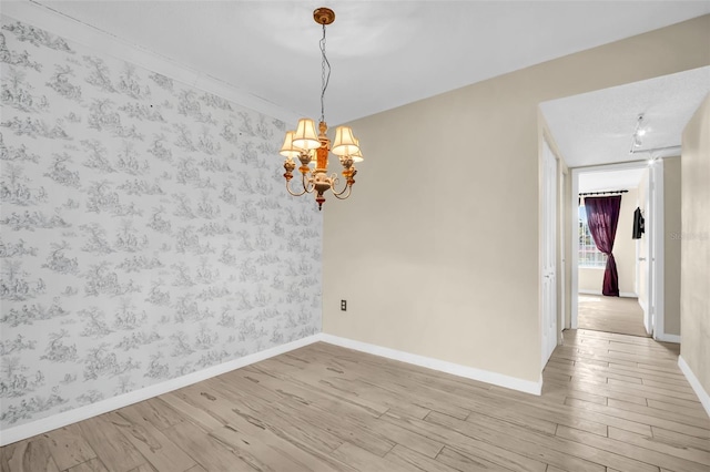 empty room featuring wood finished floors, wallpapered walls, a chandelier, and baseboards
