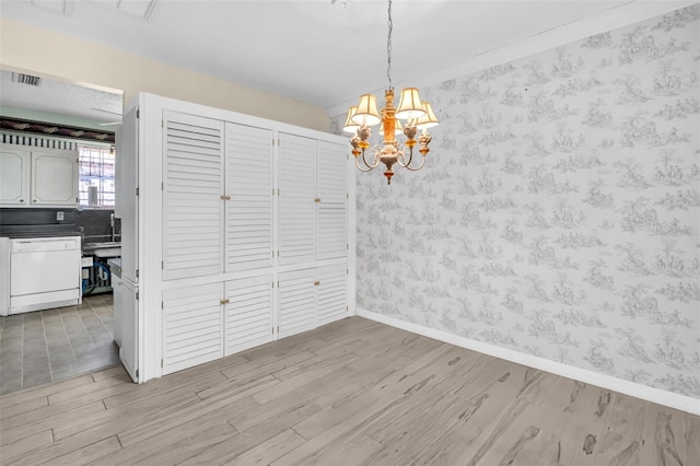 unfurnished dining area featuring wallpapered walls, light wood-style floors, a chandelier, and baseboards