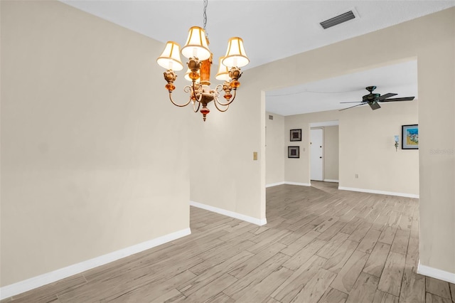 empty room with a chandelier, light wood-style floors, ceiling fan, and baseboards