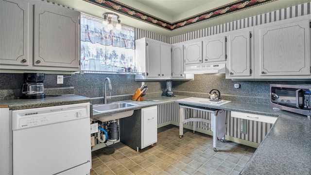 kitchen with white dishwasher, under cabinet range hood, stainless steel microwave, a sink, and dark countertops
