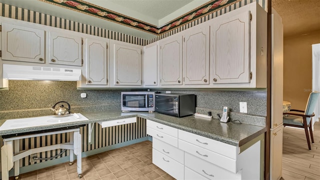 kitchen with under cabinet range hood, stainless steel microwave, black microwave, backsplash, and white electric cooktop
