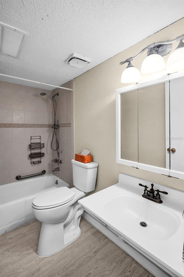 bathroom with a sink, toilet, wood finished floors, tub / shower combination, and a textured ceiling