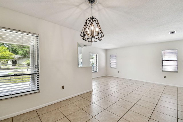 empty room featuring baseboards, visible vents, light tile patterned floors, and an inviting chandelier