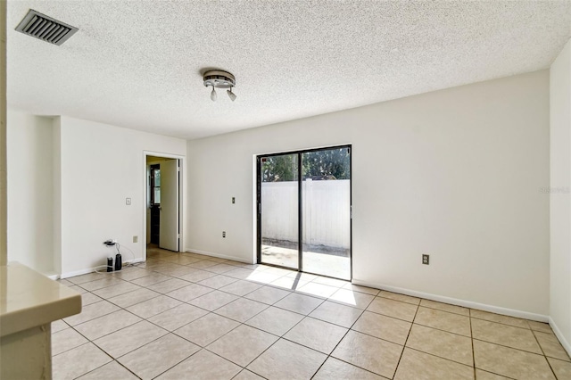 empty room with baseboards, visible vents, light tile patterned floors, and a textured ceiling
