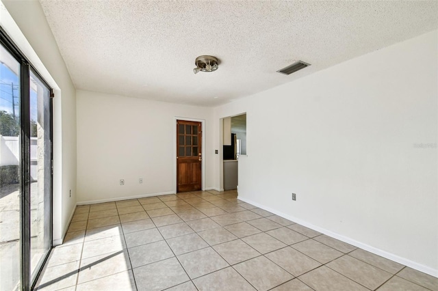 empty room featuring light tile patterned floors, a textured ceiling, visible vents, and baseboards