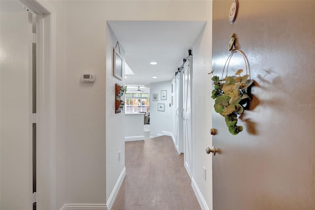 corridor with wood finished floors, a barn door, recessed lighting, and baseboards
