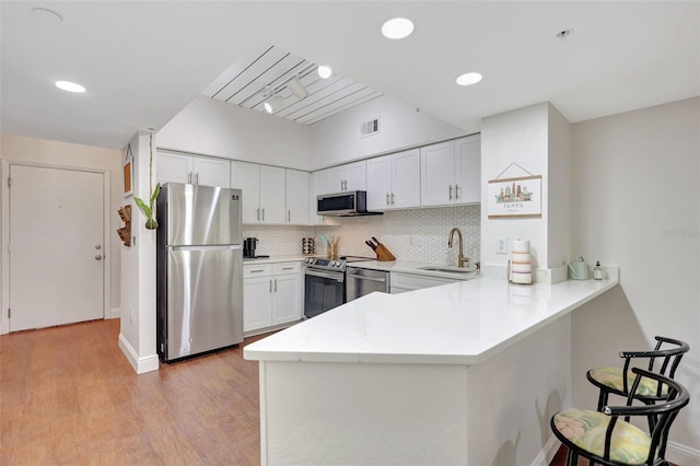 kitchen with a sink, stainless steel appliances, a kitchen bar, light wood-style flooring, and a peninsula