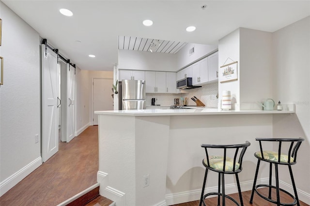 kitchen with wood finished floors, a breakfast bar area, a barn door, stainless steel appliances, and a peninsula