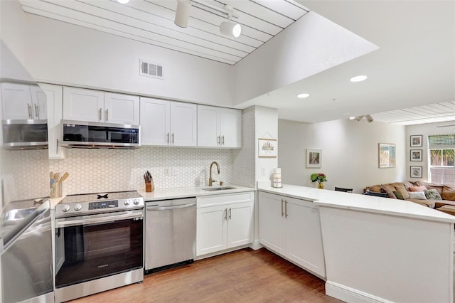 kitchen with stainless steel appliances, light wood-type flooring, a sink, visible vents, and a peninsula
