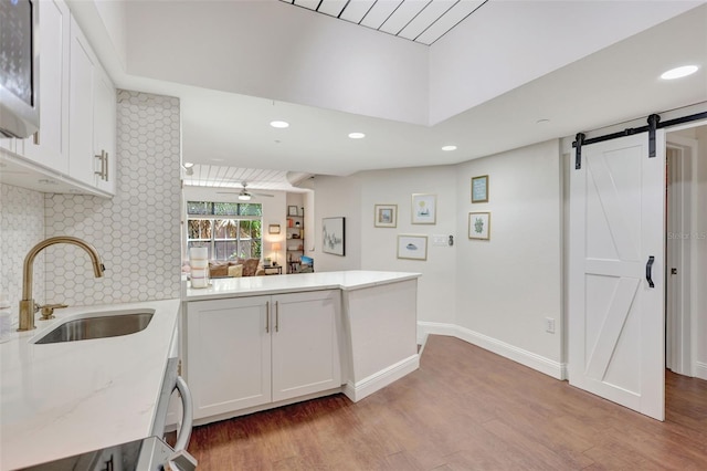 interior space with a barn door, light countertops, a sink, white cabinetry, and a peninsula