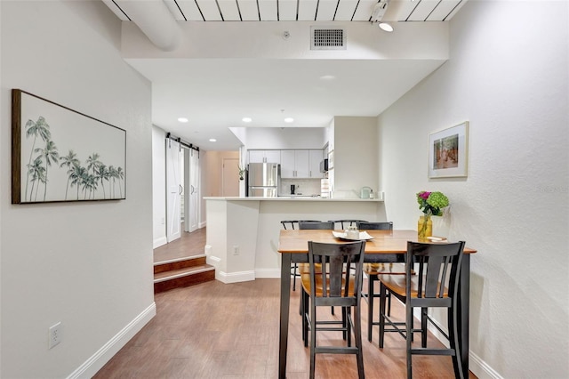 dining room featuring baseboards, visible vents, a barn door, and light wood-style flooring