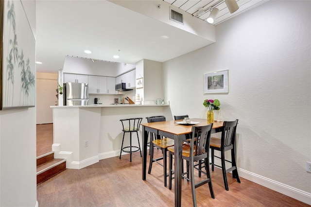 dining room with visible vents, light wood-type flooring, track lighting, and baseboards