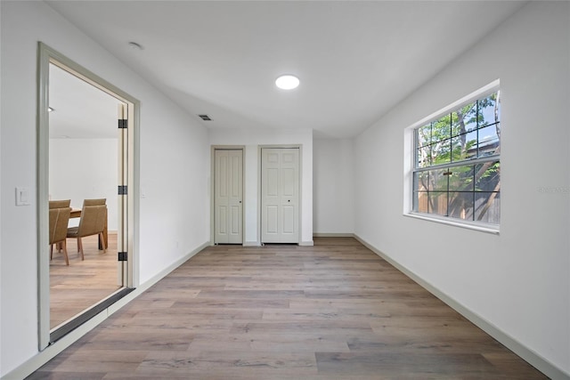 unfurnished bedroom with two closets, wood finished floors, and baseboards