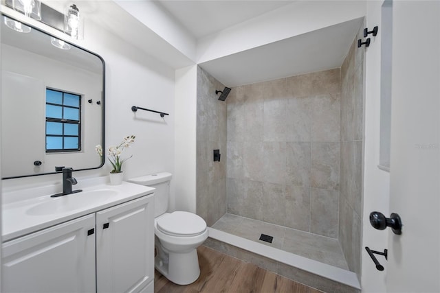 full bathroom with toilet, a tile shower, vanity, and wood finished floors