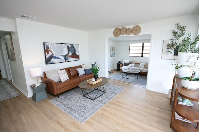 living area with baseboards, light wood finished floors, and visible vents