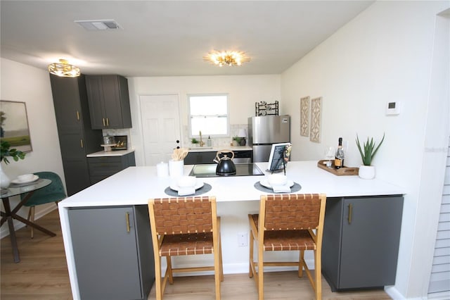 kitchen with light countertops, a breakfast bar area, freestanding refrigerator, a peninsula, and visible vents