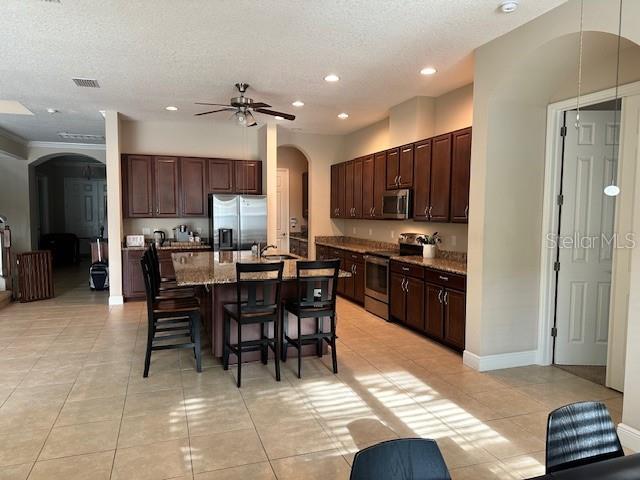 kitchen featuring stainless steel appliances, ceiling fan, a kitchen bar, arched walkways, and light tile patterned floors