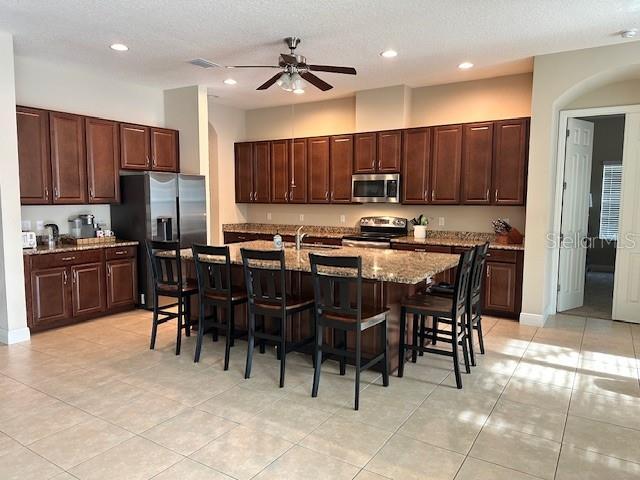 kitchen featuring a ceiling fan, a kitchen bar, an island with sink, stainless steel appliances, and recessed lighting