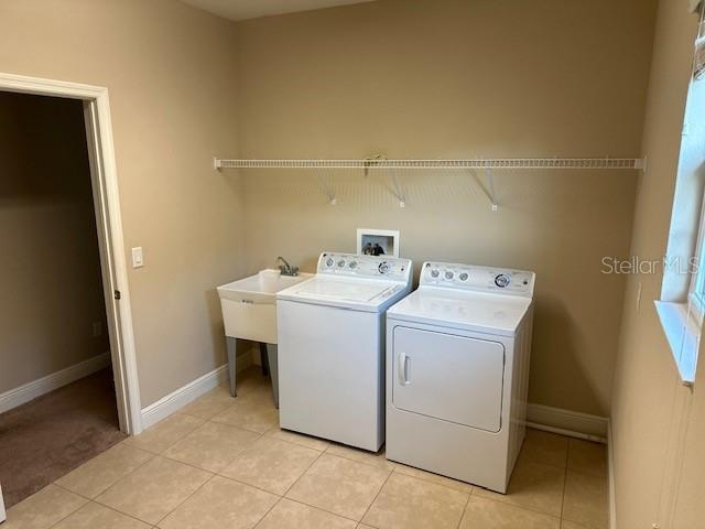 washroom with washing machine and clothes dryer, laundry area, light tile patterned flooring, and baseboards