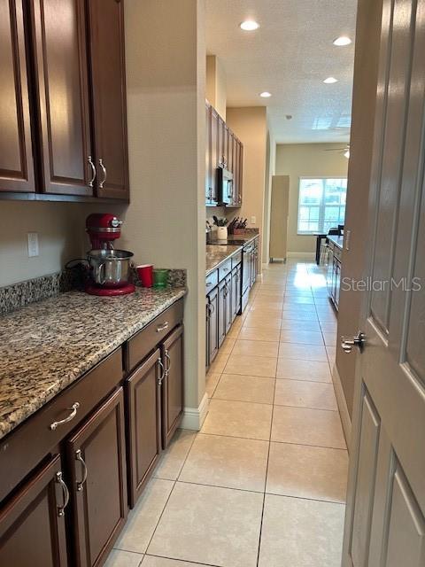 kitchen featuring recessed lighting, light tile patterned floors, dark brown cabinets, light stone counters, and stainless steel microwave